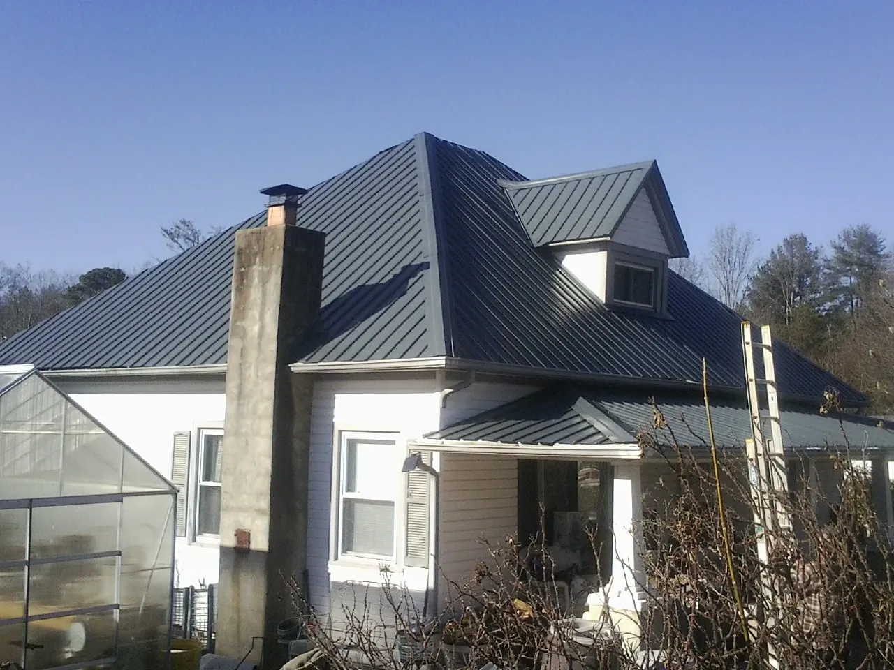 Dark blue standing seam metal roof on a white farmhouse with dormer — Slate & Tile Roof Repair by Roofing Brothers in Walstonburg