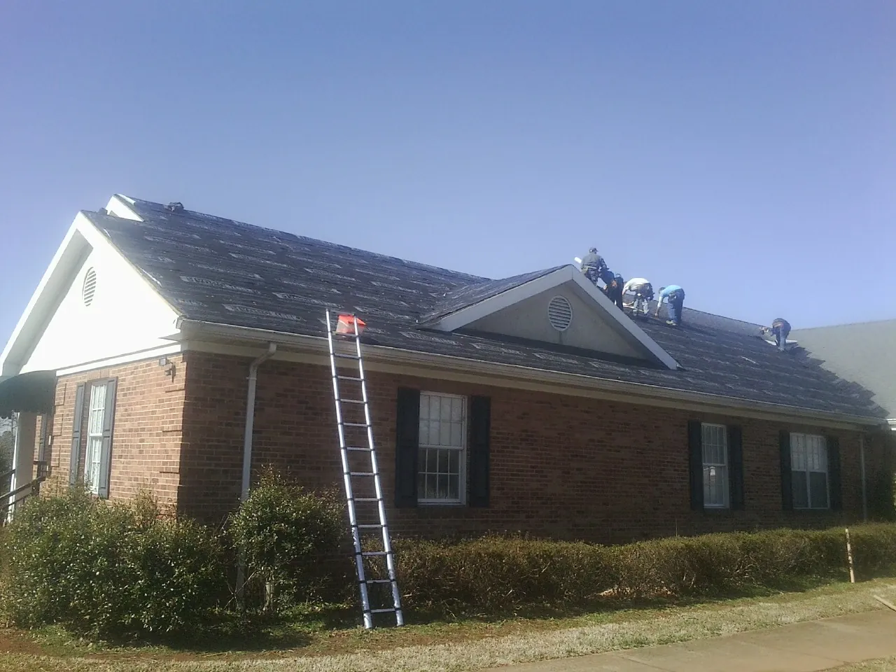 Crew tearing shingles off a brick ranch roof with a ladder set — Emergency Roof Repair work by our crew in Walstonburg