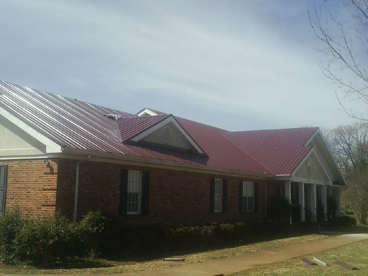Red metal roof with gabled entries on a long brick building, from a Hail Damage Roof Repair job in Walstonburg