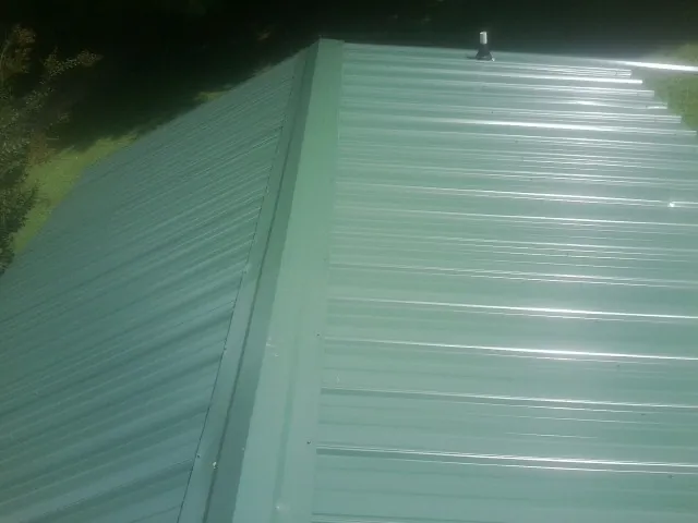 New green metal panels meeting at the ridge of a roof — Flat Roof Repair work by our crew in Walstonburg