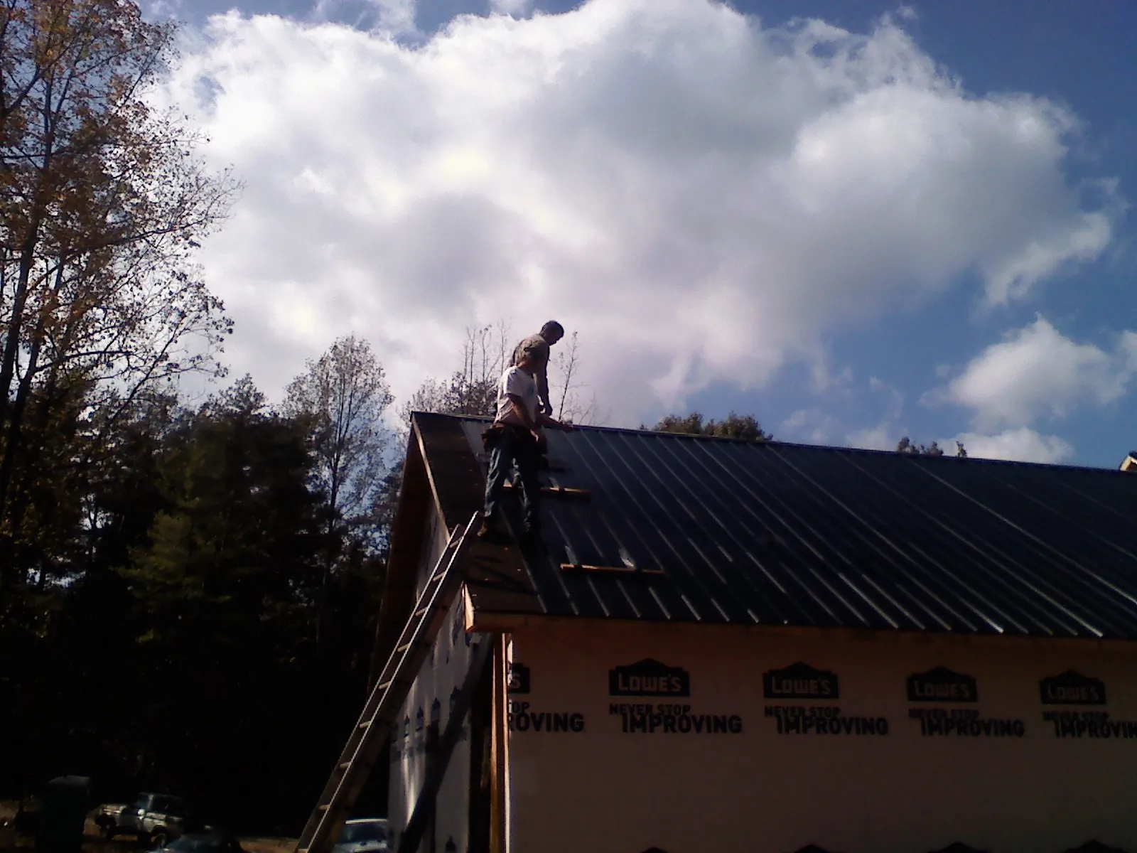 Roofer fastening dark metal panels high against a cloudy sky, from a Roof Inspection job in Walstonburg