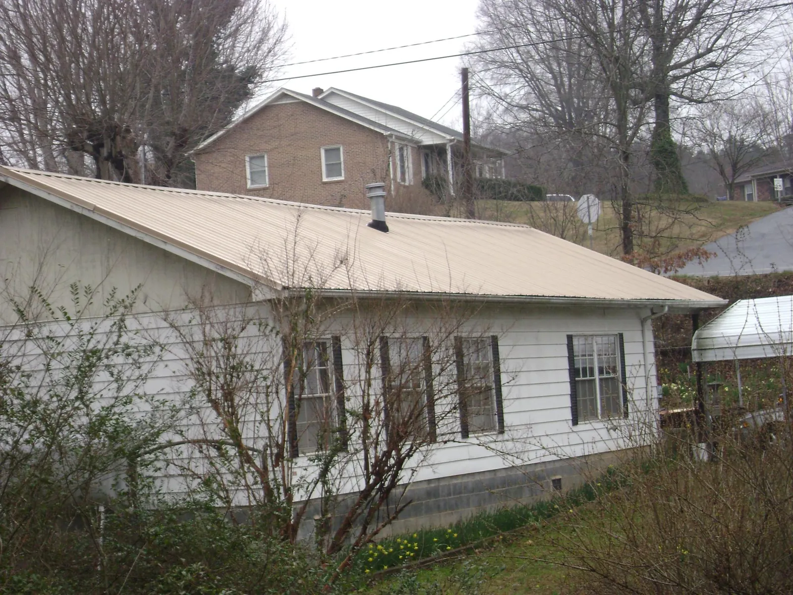 Tan metal roof on a white sided house set into a hillside — Commercial Roofing by Roofing Brothers in Walstonburg